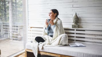 a woman sits with coffee and a book in her home wondering how long does a furnace last