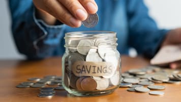 woman-putting-coins-in-a-jar-labled-savings