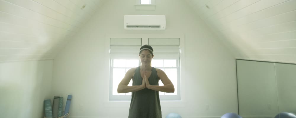 A women doing yoga in a room with a mini split ac system installed on the wall.