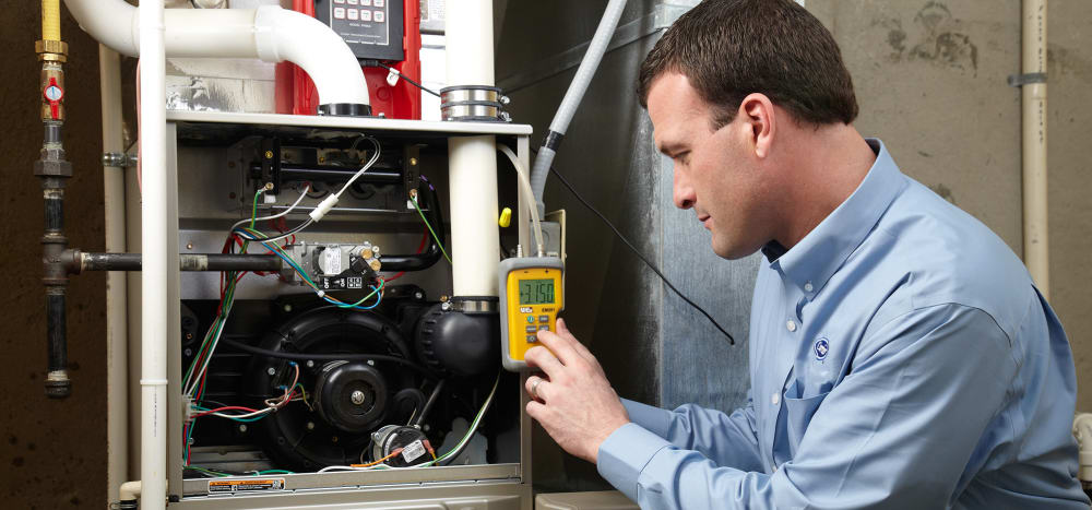 A Carrier technician using tools on a furnace to explain how a gas furnace works to a homeowner