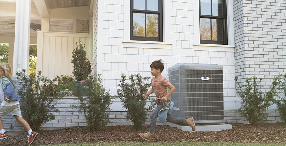 a boy runs outside by a 4 ton ac unit