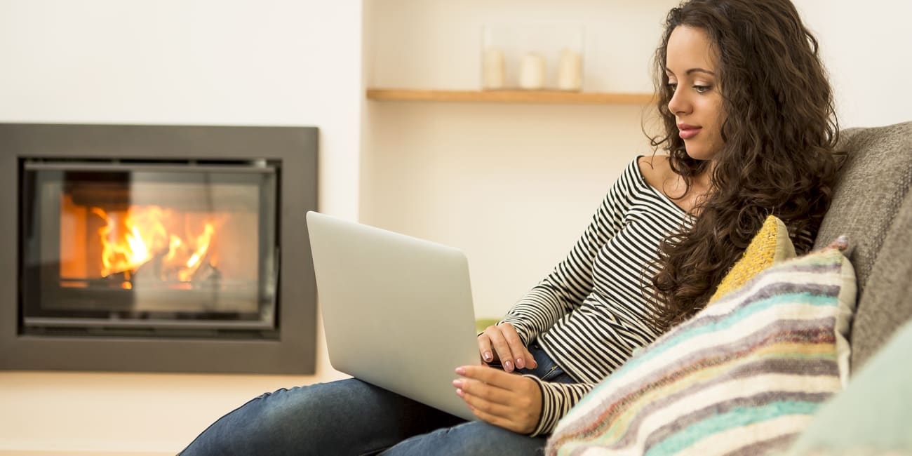 woman researches smart thermostats on laptop by fireplace