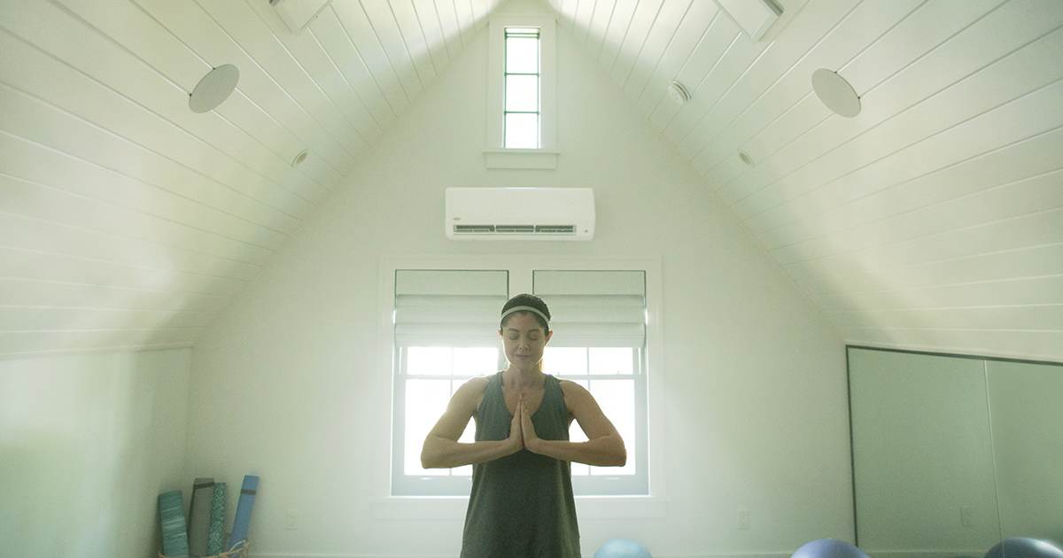 A woman doing yoga in white room with a dual zone mini split installed.