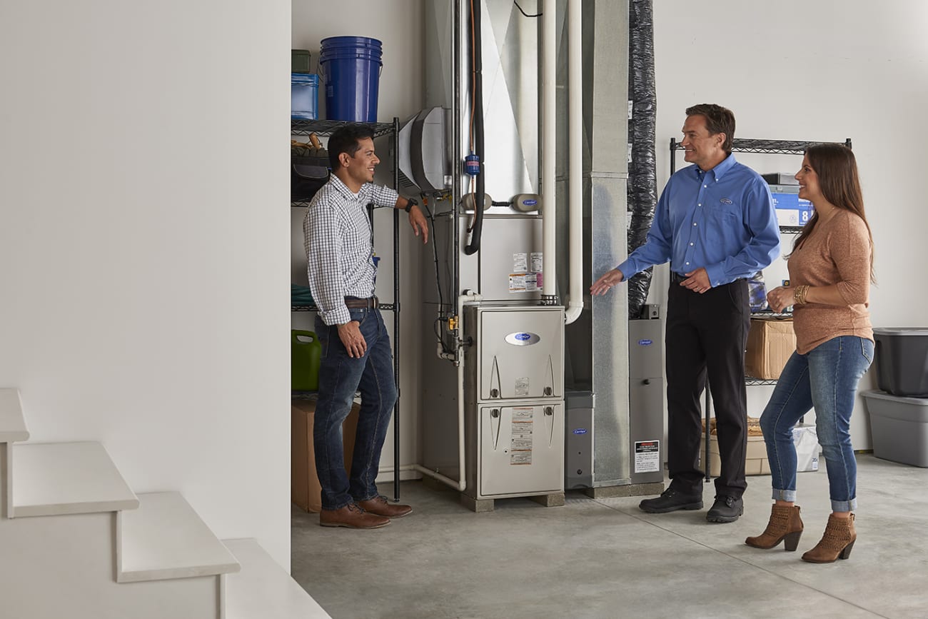 A Carrier dealer standing near a furnace explaining to a couple what is merv rating.