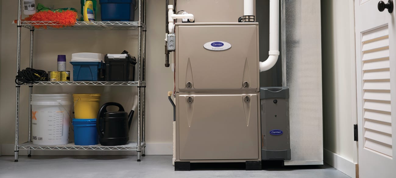 A Carrier Infinity home furnace installed in a garage next to wire shelving rack.