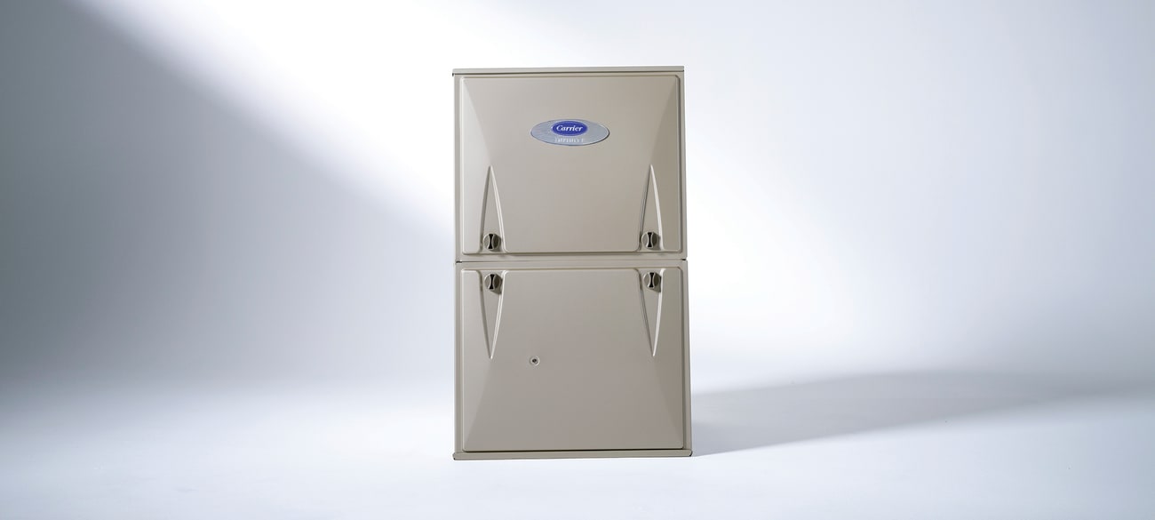 A Carrier house furnace sitting in a white room with lighting causing shadows.
