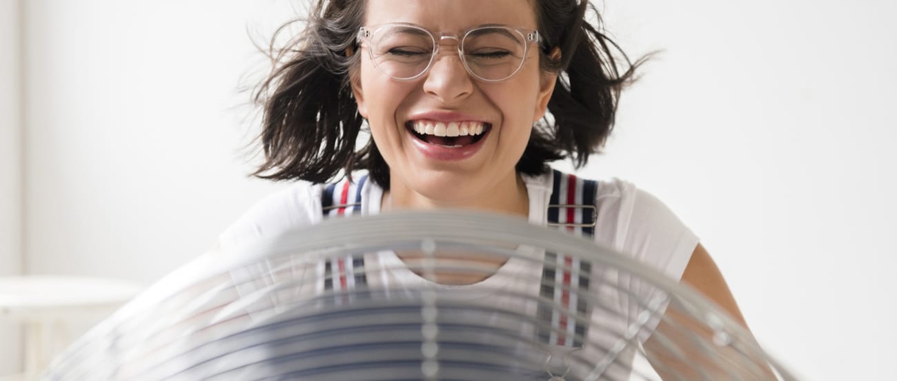 a woman without house ac sits in front of a fan after learning how does air conditioning work in air conditioning systems