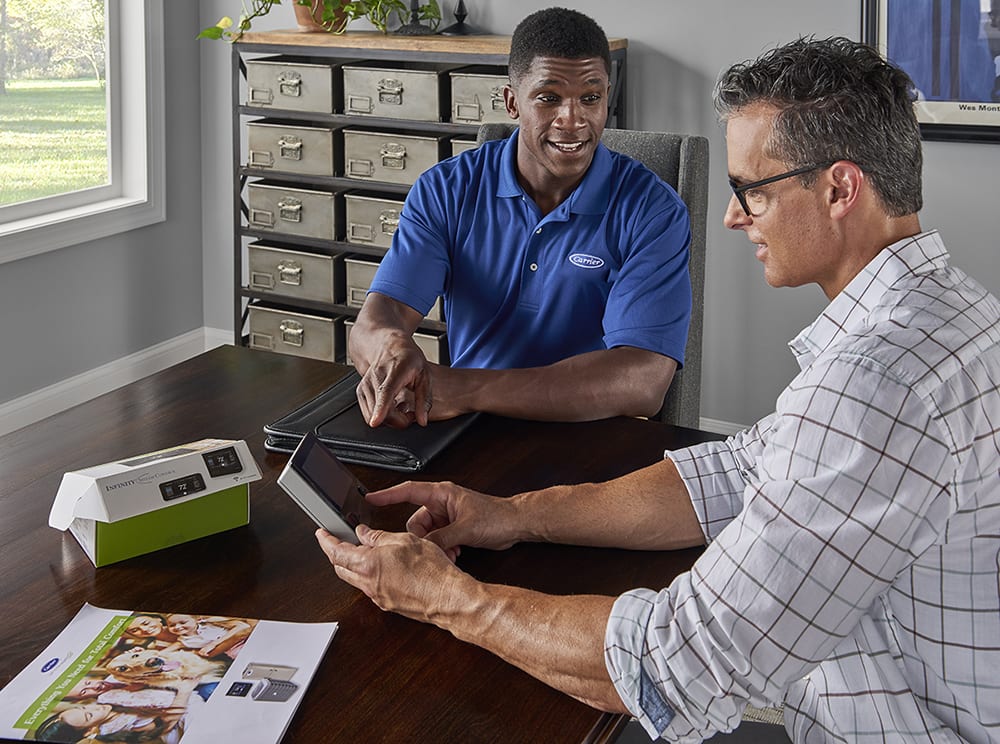 a carrier dealer explains best smart thermostat and wifi thermostat options to a man at table