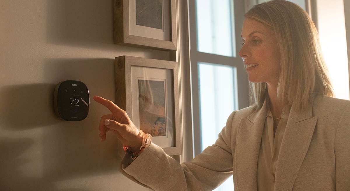 a woman sets the temperature on the best wifi thermostat for her home