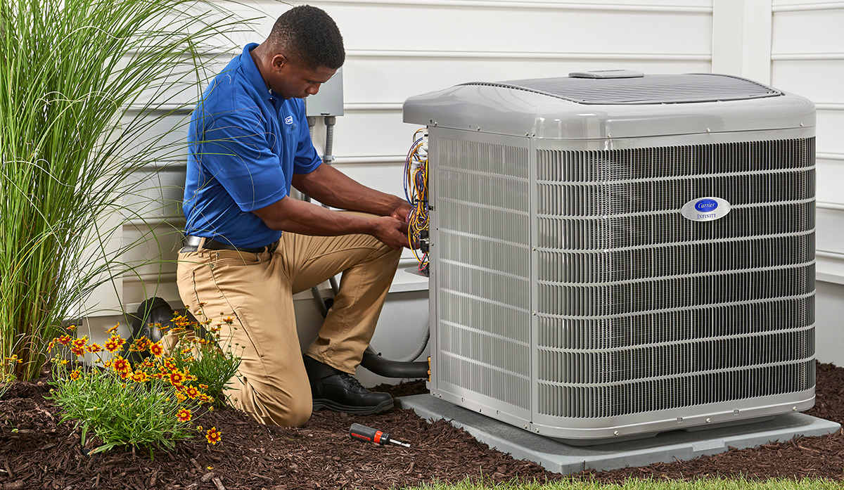 a carrier dealer services an air conditioner condenser unit outside of a home