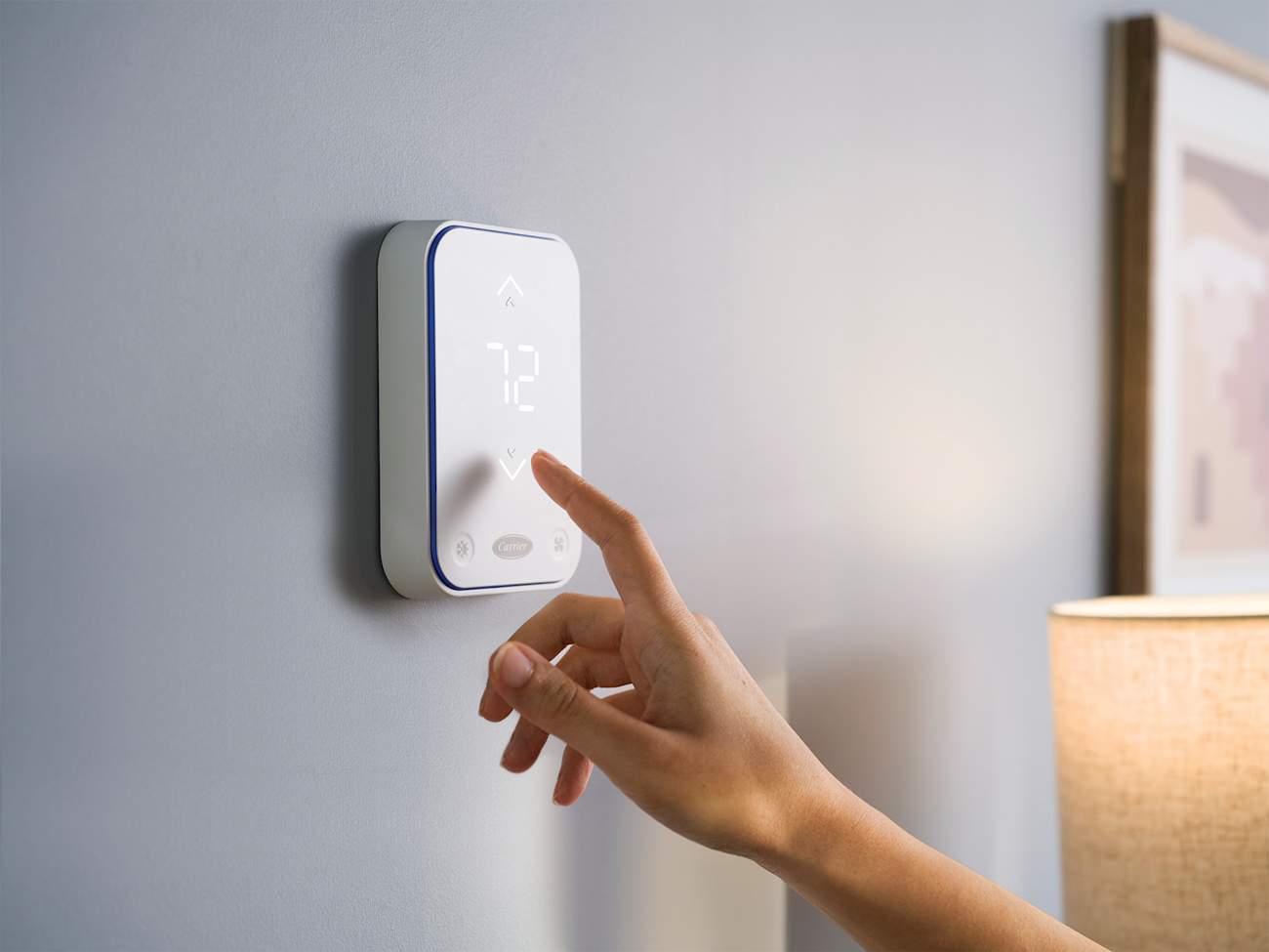 woman adjusting temperature of the carrier hvac smart thermostat on grey wall