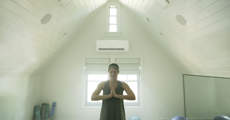 A woman doing yoga in white room with a dual zone mini split installed.