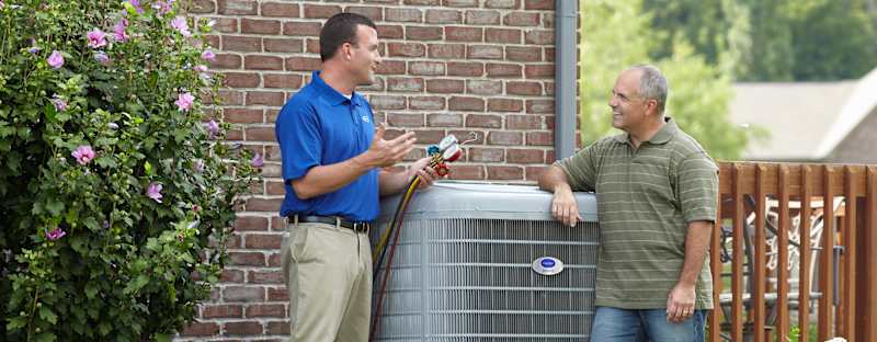 a carrier technician standing by a high efficient heat pump helps a man understand heat pump SEER rating