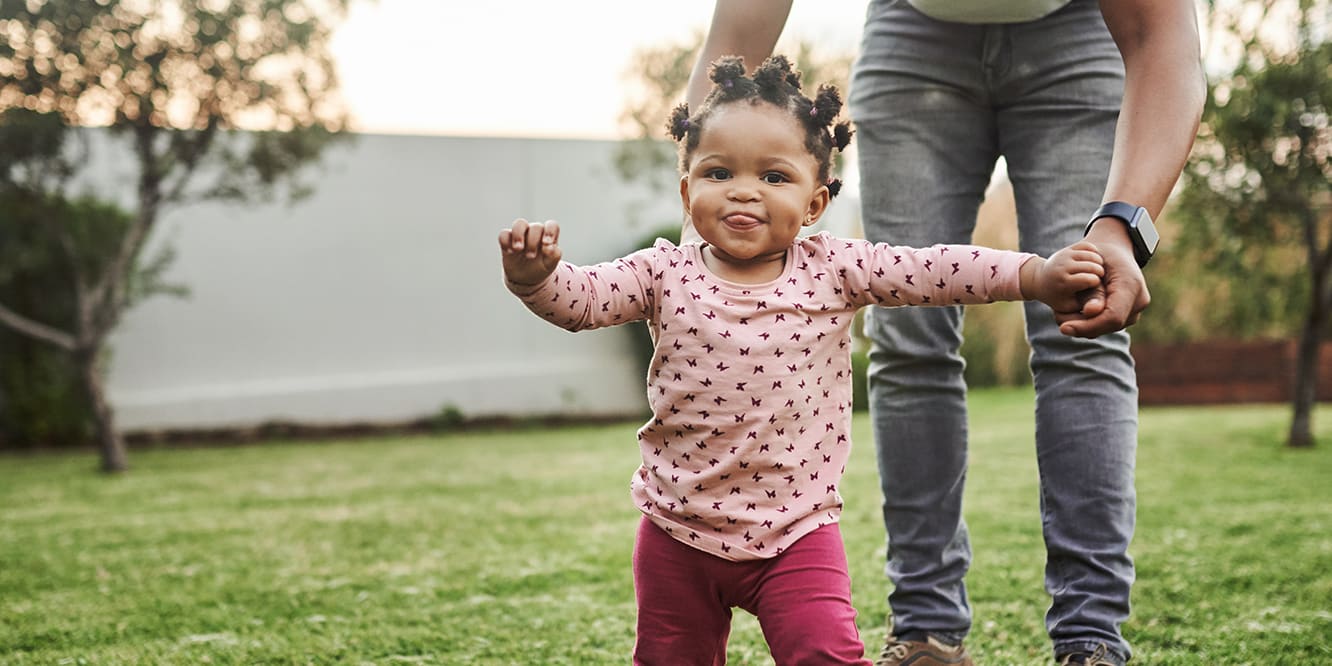 toddler-standing-in-backyard-with-help-of-parent-3x2