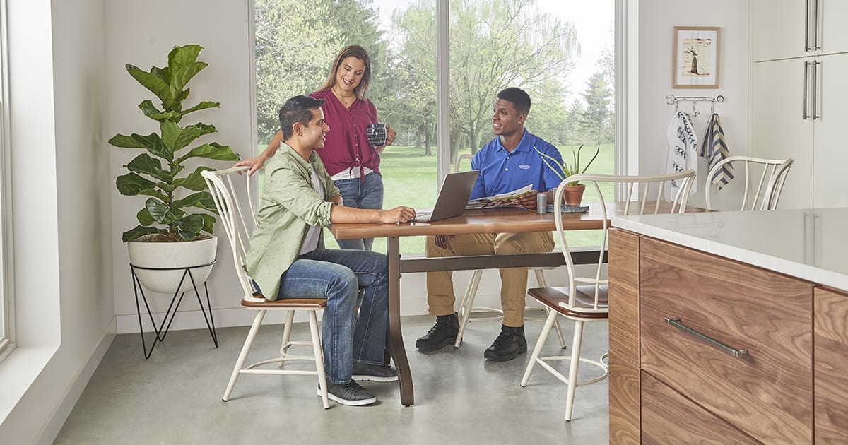 hvac-dealer-discusses-central-air-conditioner-prices-with-homeowners-in-kitchen An HVAC dealer discusses-central air conditioner prices with homeowners in kitchen.