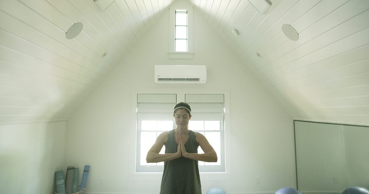 A woman doing yoga in white room with a dual zone mini split installed A woman doing yoga in white room with a dual zone mini split installed.