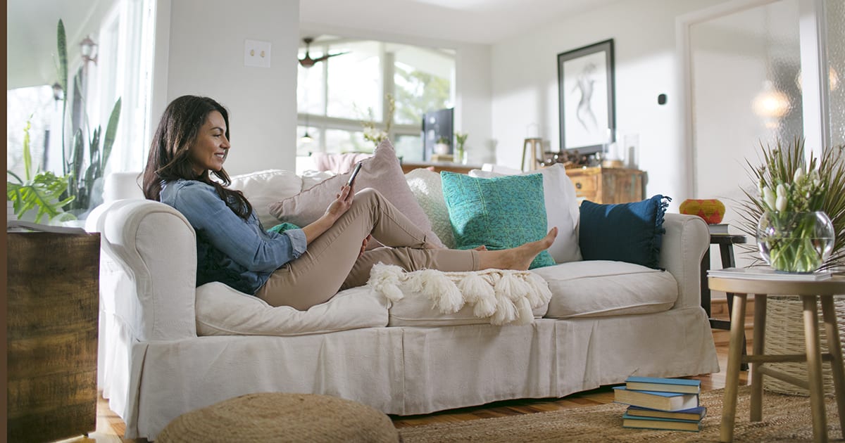 A woman sitting on a couch researching how do smart thermostats work A woman sitting on a couch researching how do smart thermostats work