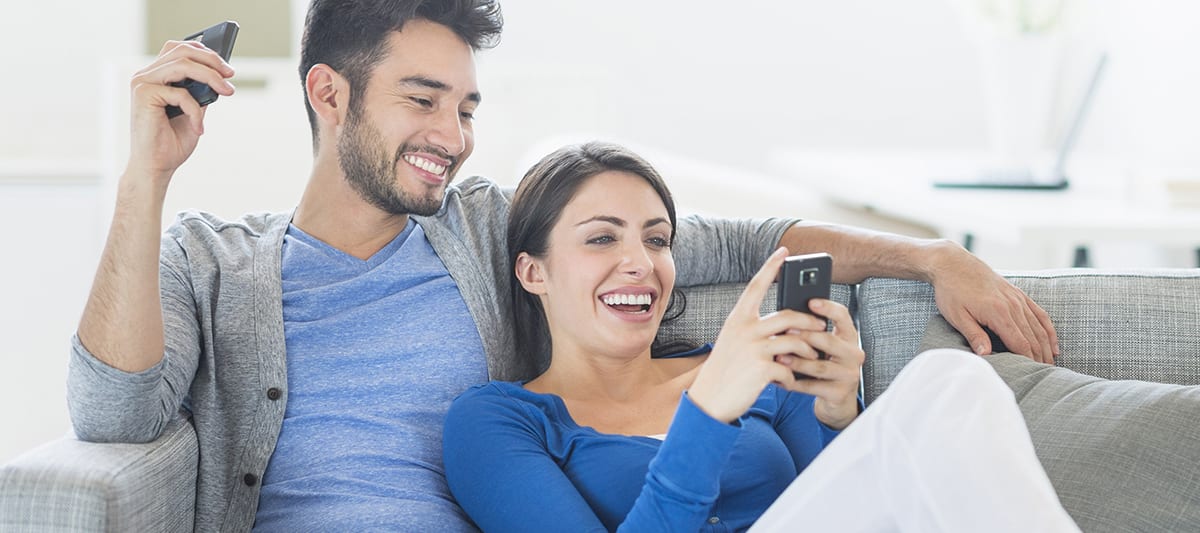 man and woman on couch looking at stale air causes on phone man and woman on couch looking at stale air causes on phone
