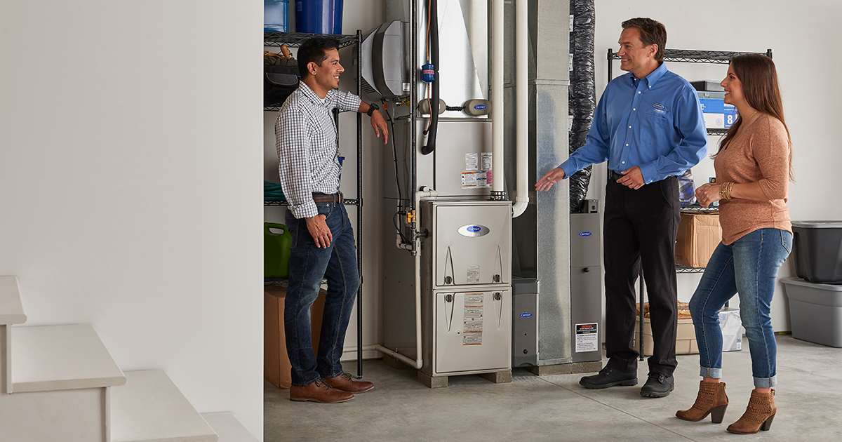 a carrier dealer discusses furnace blower replacement cost with homeowners in basement a carrier dealer discusses furnace blower replacement cost with homeowners in basement