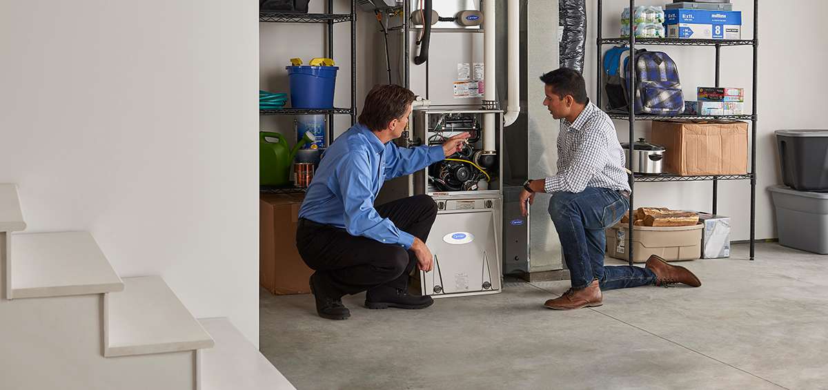 a carrier furnace installer explains the furnace install process to a man kneeling by furnace a carrier furnace installer explains the furnace install process to a man kneeling by furnace