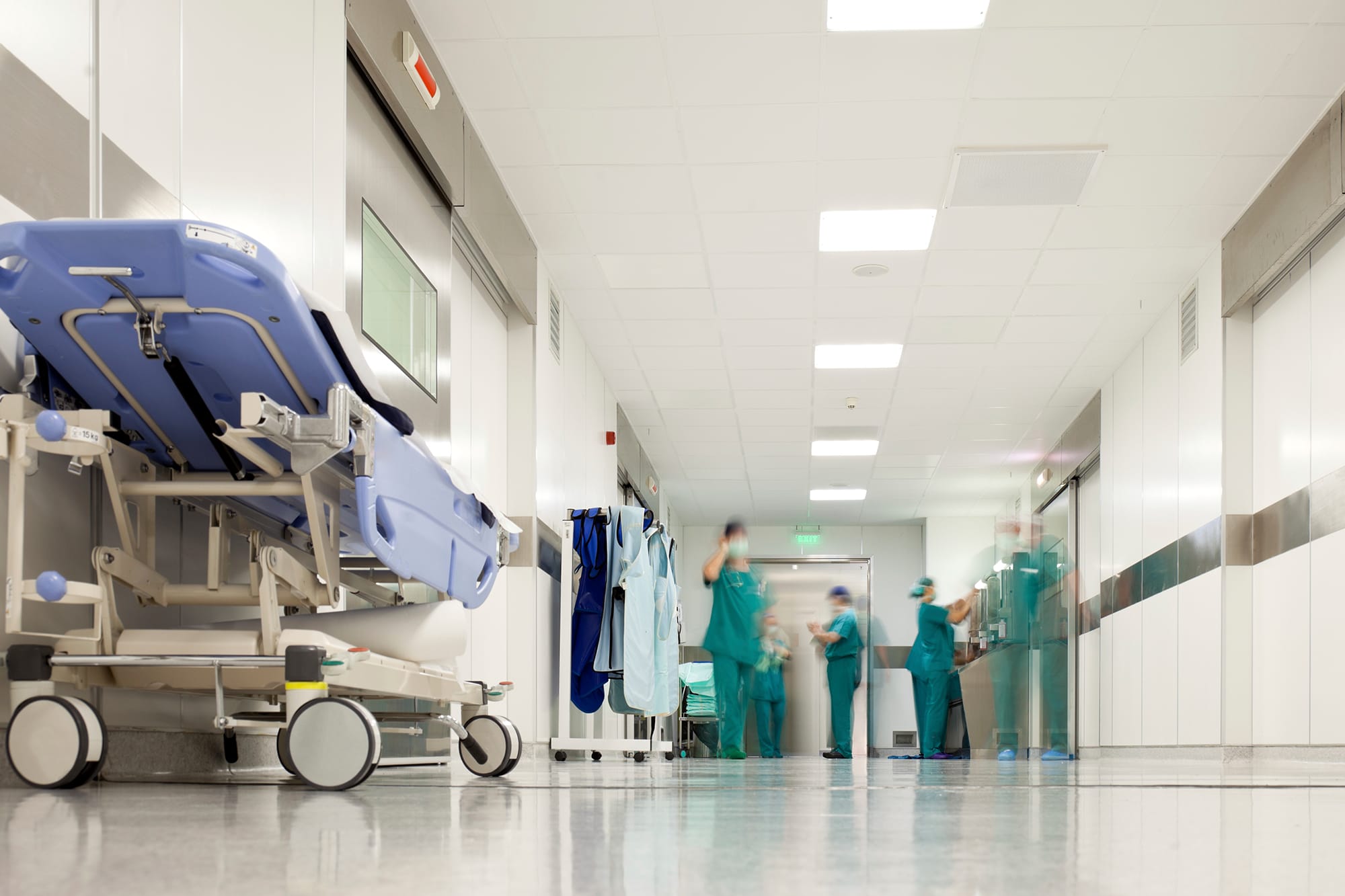 A photo of hospital corridor with a hospital bed and personnel walking by A photo of hospital corridor with a hospital bed and personnel walking by