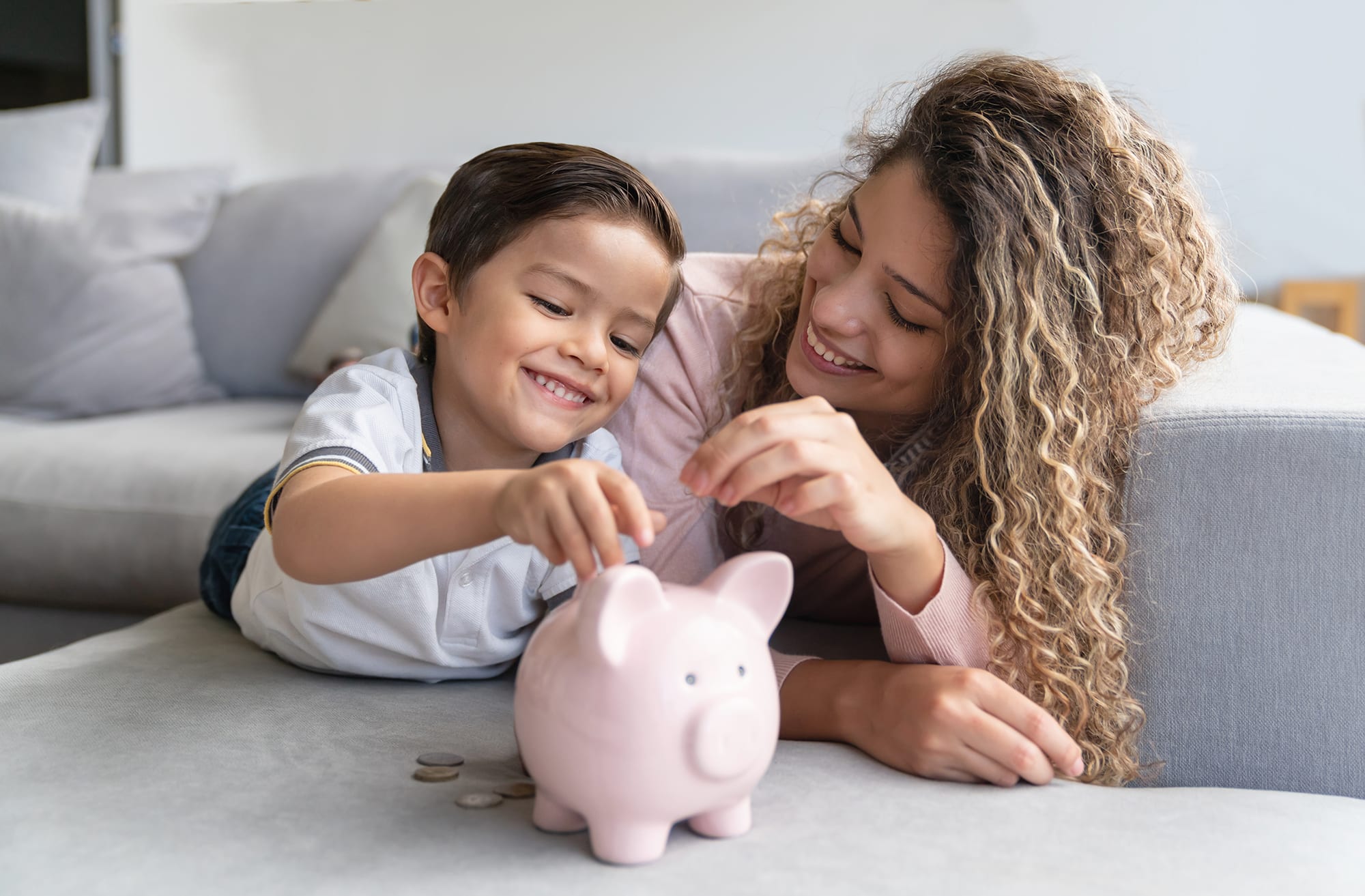  A mother and her child are smiling while putting coins into a piggy bank.