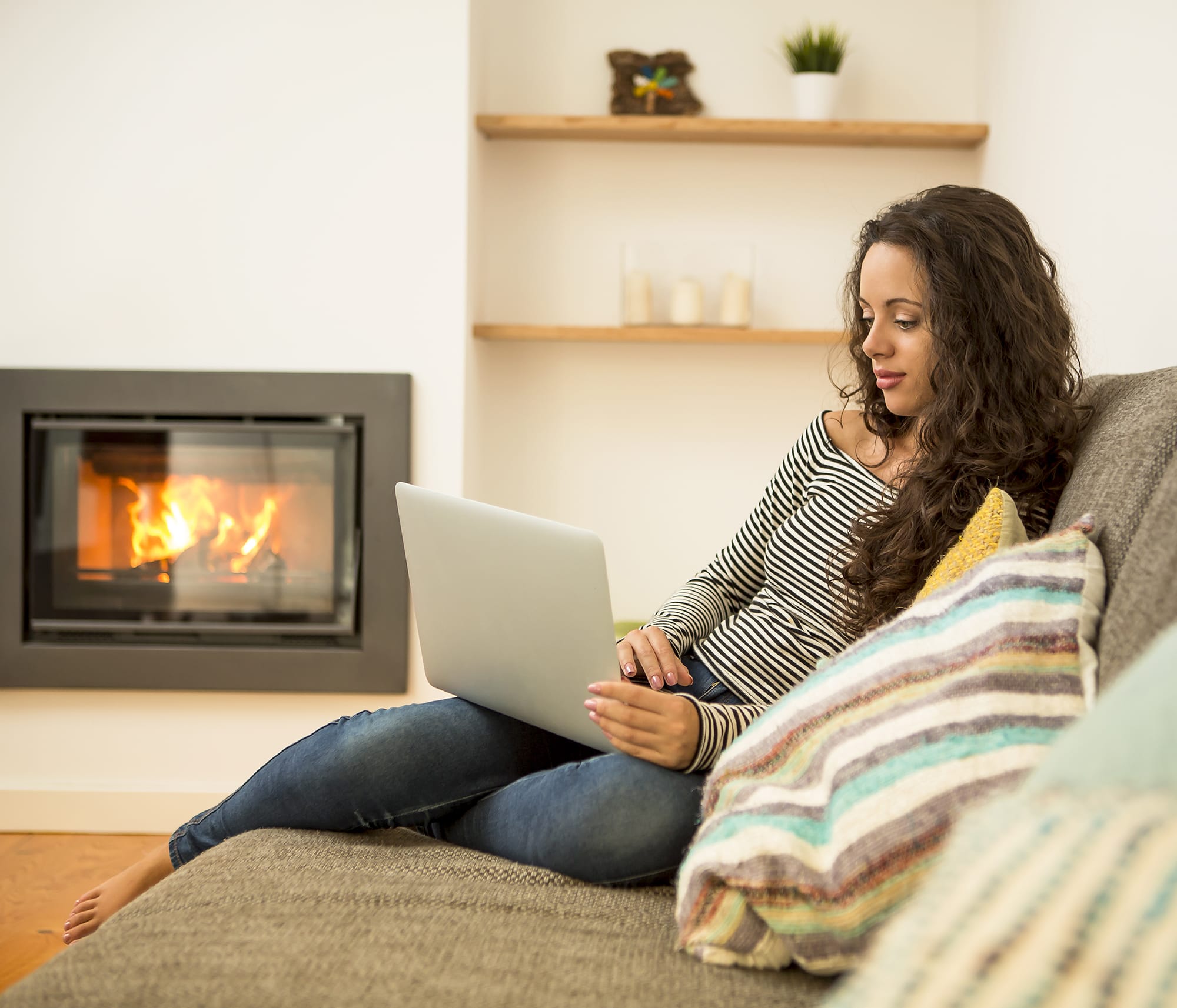 woman researches smart thermostats on laptop by fireplace
