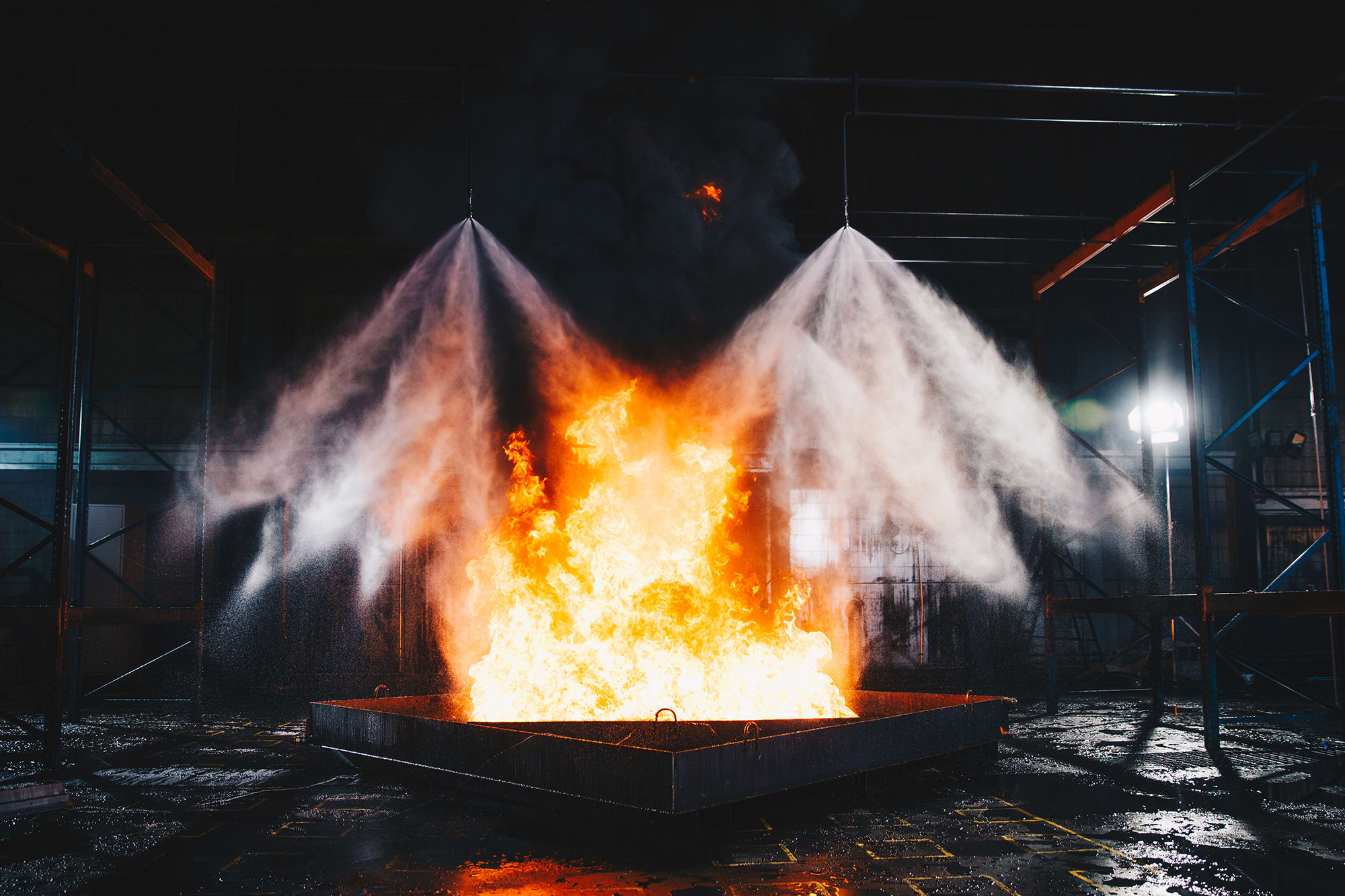 Marioff high-pressure water mist discharge from two spray heads over flames in fire test permises.