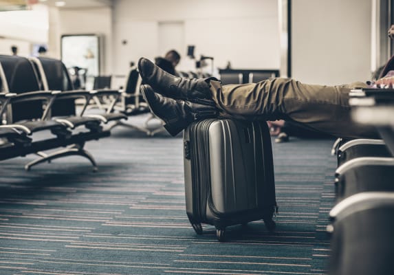mans-legs-resting-on-suitcase-in-airport-waiting-lounge