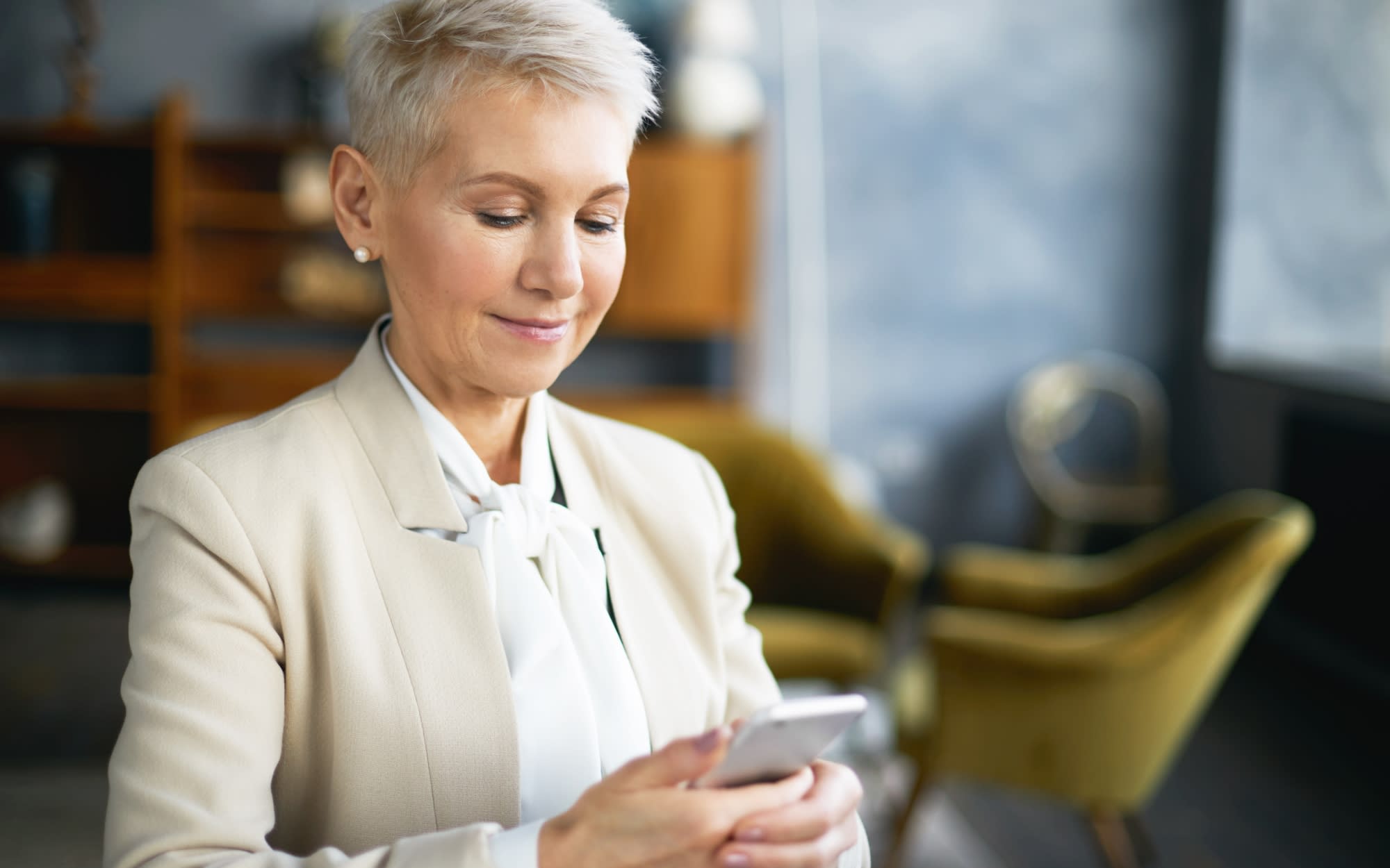 Close up of mature female real estate agent smiling while looking at mobile app