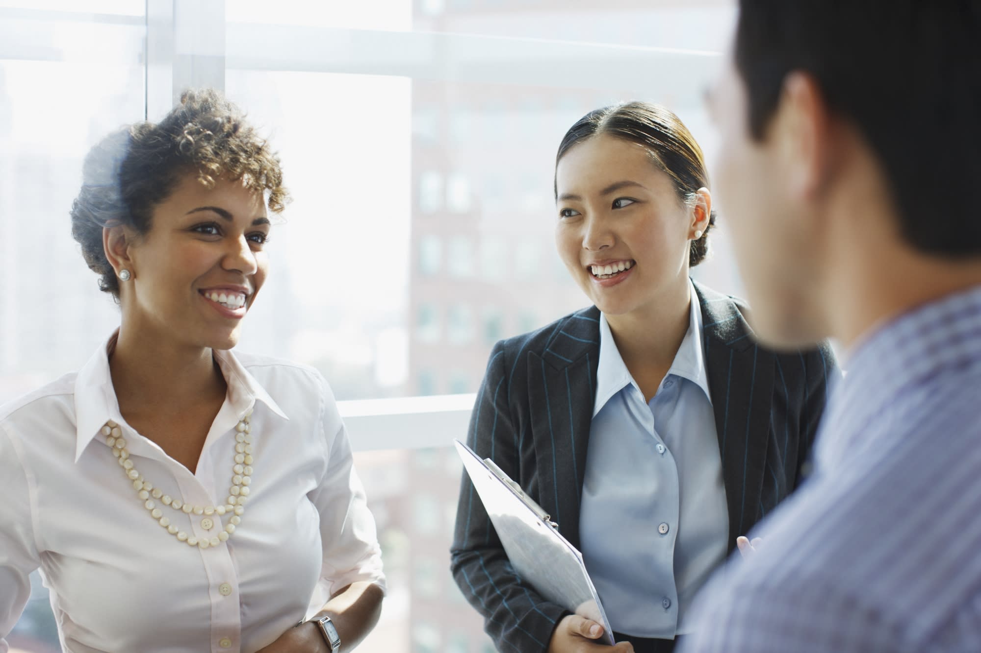 Close up of three young professionals dressed in business attire collaborating and smiling