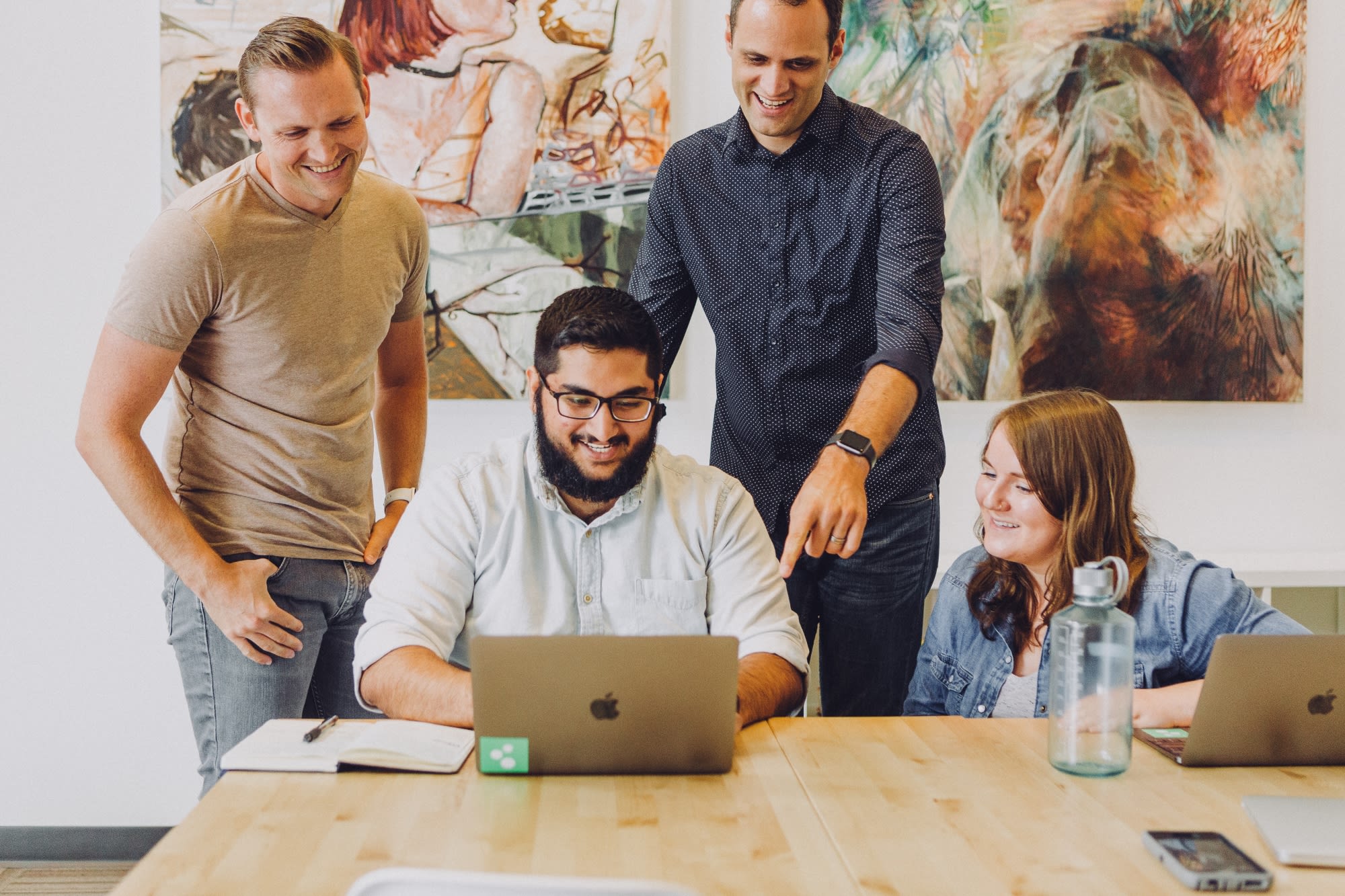 Four young casual professionals gathered around wood table looking at laptop computer