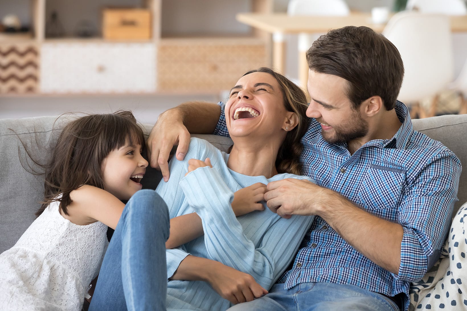 family-sitting-on-couch-in-living-room-have-fun-little-daughter-tickling-mother-3x2