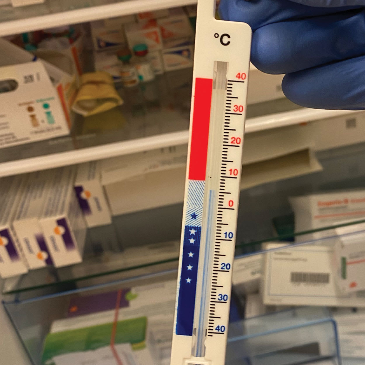 Thermometer reading 5°C in front of refrigerator filled with vaccines