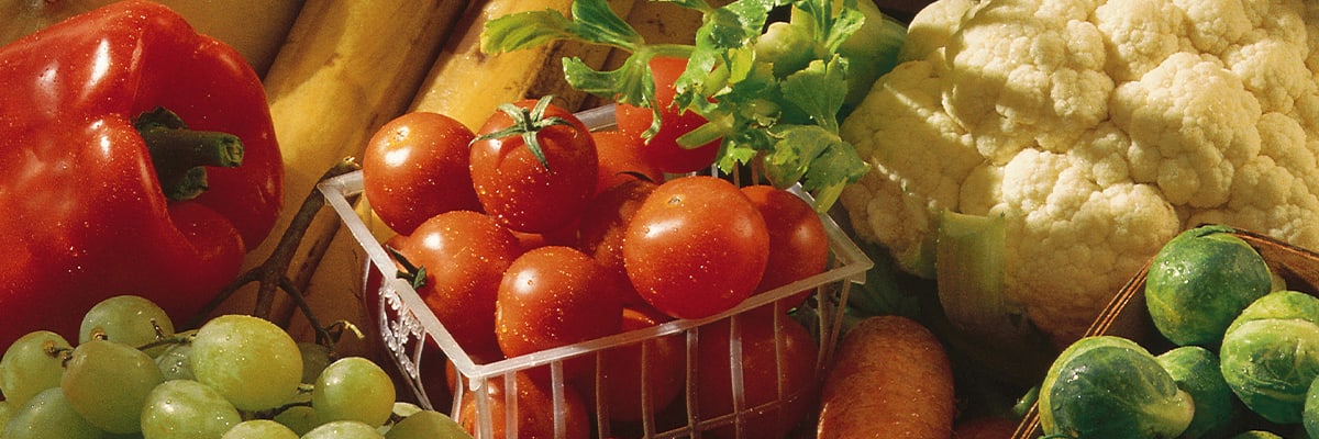 Tomatoes in plastic basket in front of mixed fruits and vegetables